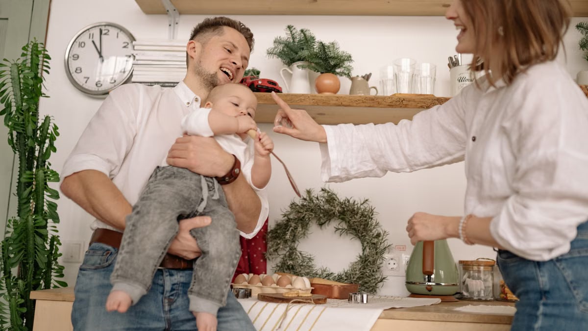 A joyful family moment capturing parents and baby in a cozy kitchen setting.