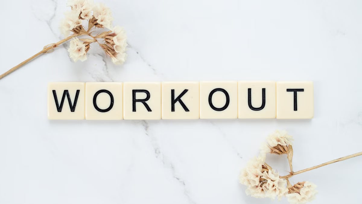 Letter tiles spelling 'WORKOUT' on marble with dried flowers, conveying fitness motivation.